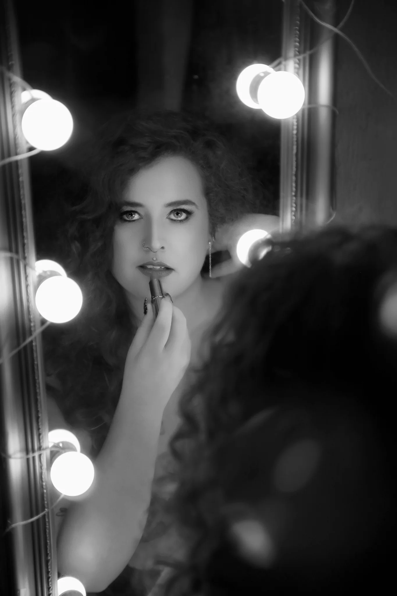 Black and white boudoir portrait at a lit vanity mirror
