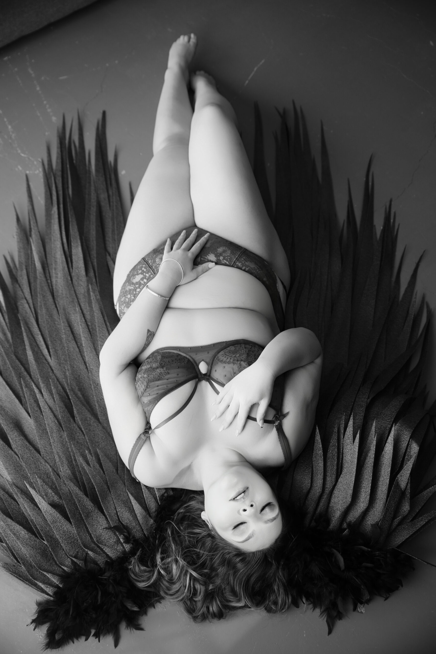 Curvy woman lying on black feather wings, black and white boudoir photography Melbourne